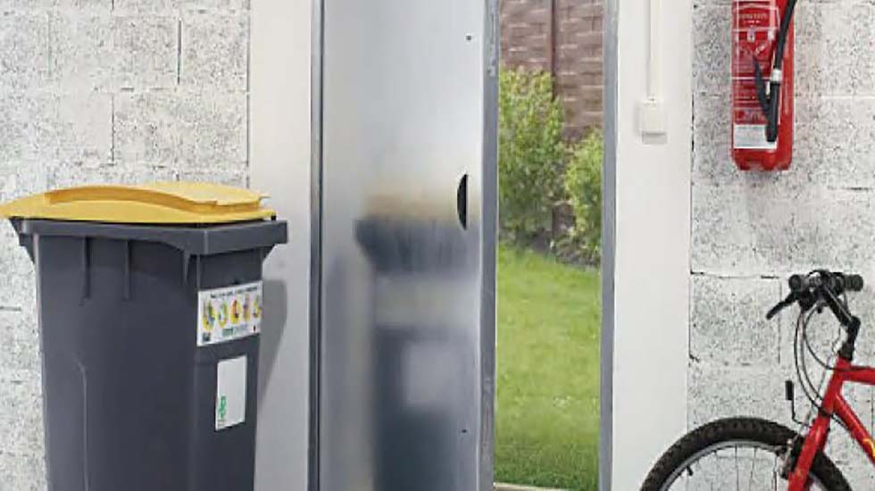 A reflective stainless steel door with a vandal-resistant finish, positioned in an urban setting with a bin and bicycle nearby
