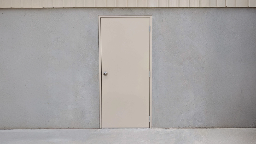 Beige personal access door installed on a grey concrete building, showing a standard installation setup