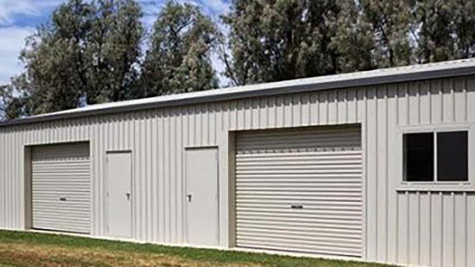 Large metal shed with personal access doors and roller doors, surrounded by trees in a rural setting.