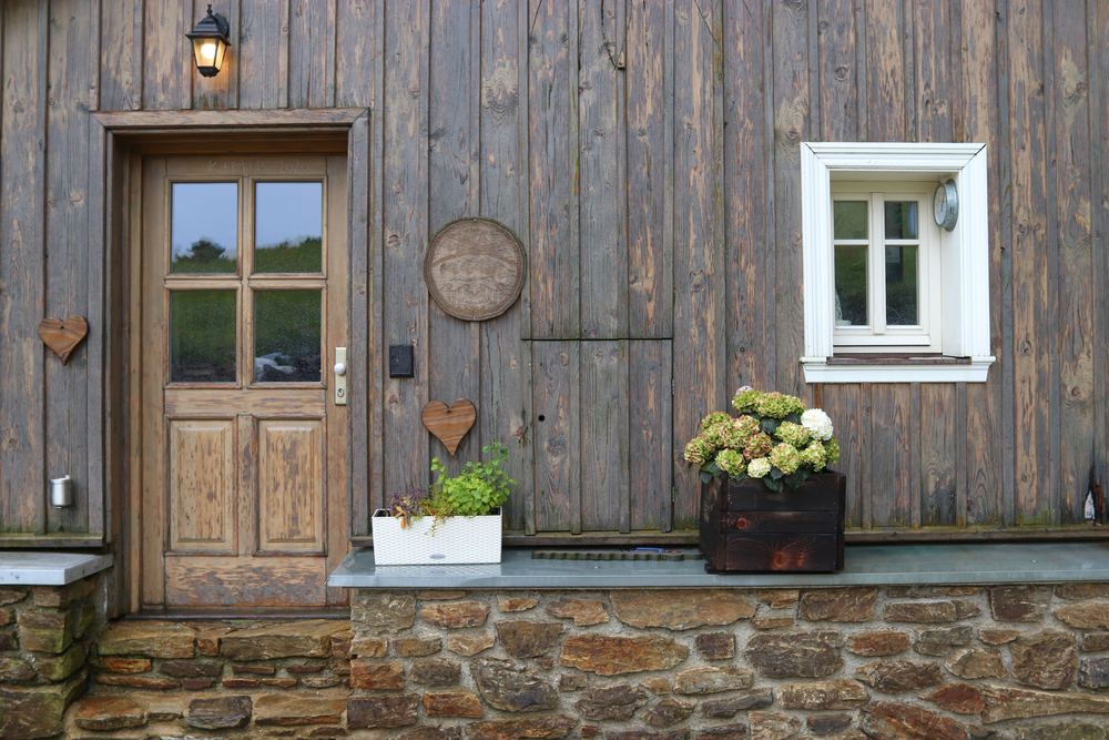 Rustic exterior of a house with a wooden door, stone pathway, and potted plants, showcasing a classic farmhouse design