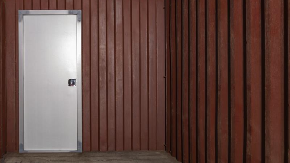 White metal personal access door with a secure lock, installed in a red corrugated container wall—designed for durability and security in industrial and mining environments