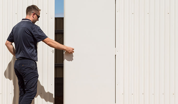 A worker opening a steel-clad door set into the exterior of a building.